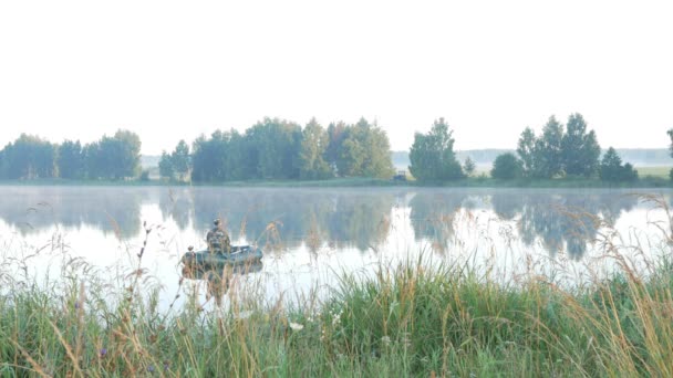 Uppblåsbar båt med en manlig fiskare på en sjö i dimman. Tidigt på morgonen. — Stockvideo