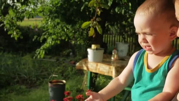 Mutter und kleiner Junge auf der Veranda des Hauses genießen die Regentropfen. der Sohn ist sehr glücklich mit dem Wasser und dem Schielen bei Sonnenuntergang — Stockvideo