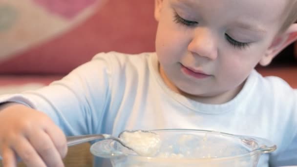 Милий маленький хлопчик їсть кашу з шматочками м'яса за дитячим столом. домашня обстановка — стокове відео