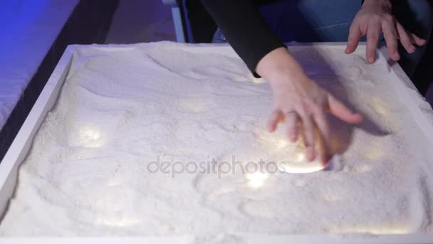 A young mother plays with her son in a salt room. Together they draw patterns on a luminous table. — Stock Video