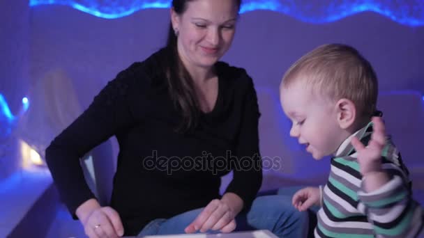 Una joven madre juega con su hijo en una sala de sal. Juntos dibujan patrones en una mesa luminosa . — Vídeos de Stock