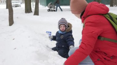 Sevimli küçük çocuk ve genç anne kış ile oyun kar parkta. Mavi çocuk ceket ve anne, kırmızı.