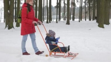 Sevimli küçük çocuk ve genç anne kış ile oyun kar parkta. Mavi çocuk ceket ve anne, kırmızı.