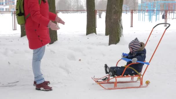 Roztomilý malý chlapce a mladá matka hrát v zimě sněhem v parku. Bunda modrá děti a červená, Máma. — Stock video