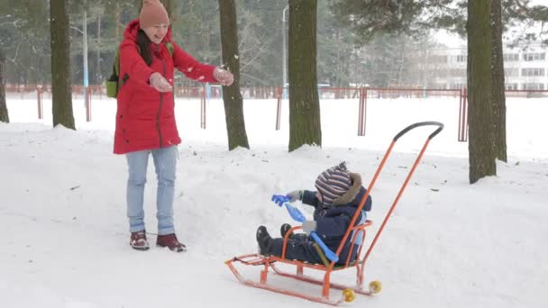 Cute little boy and young mother play in the winter with snow in the park. Blue kids jacket and red at mom. — Stock Video