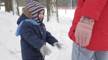 Sevimli küçük çocuk ve genç anne kış ile oyun kar parkta. Mavi çocuk ceket ve anne, kırmızı.