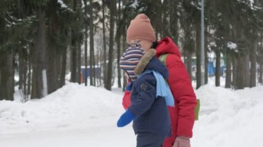 Sevimli küçük çocuk ve genç anne kış ile oyun kar parkta. Mavi çocuk ceket ve anne, kırmızı.