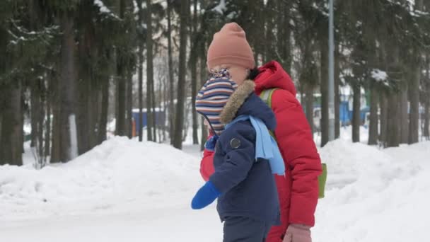 Милий маленький хлопчик і молода мати грають взимку зі снігом в парку. Синій дитячий піджак і червоний на мамі . — стокове відео