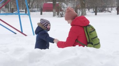 Sevimli küçük çocuk ve genç anne kış ile oyun kar parkta. Mavi çocuk ceket ve anne, kırmızı.
