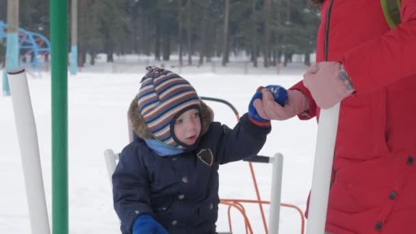 Un niño lindo y una madre joven se dedican a los equipos de ejercicio al aire libre. Es difícil para un niño llegar a las asas de los equipos — Vídeos de Stock