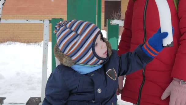En söt liten pojke och en ung mamma är engagerade i utomhus träningsutrustning. Det är svårt för ett barn att nå handtagen på utrustning — Stockvideo