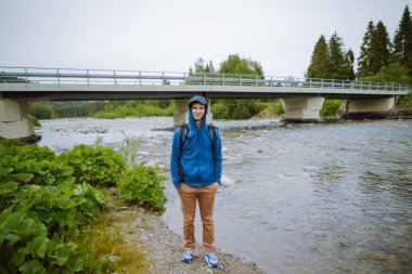 Erkek turist dağ nehrinin yanında duruyor.
