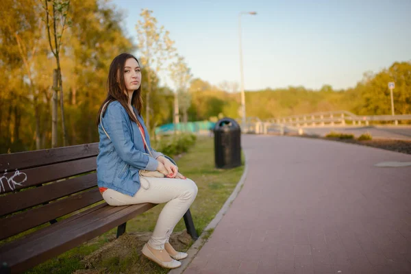 Den vackra unga stadskvinnan sitter på en bänk — Stockfoto