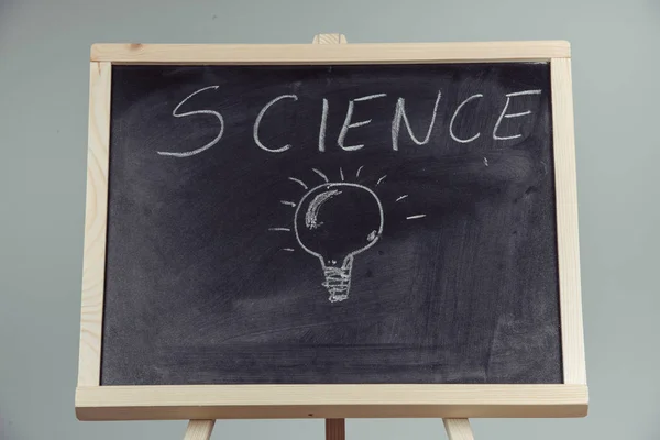 A teacher writing science, drawing chemistry elements on dark chalkboard by hand