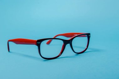 Mavi arka planda kırmızı plastik çerçeveli gözlük.