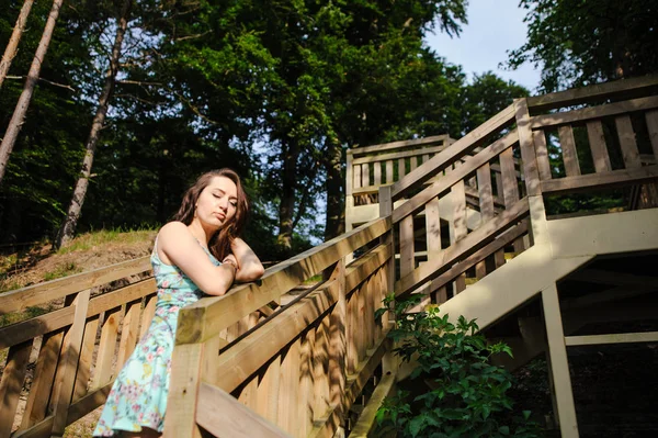 Девушка сидит на деревянной лестнице в парке и улыбается — стоковое фото
