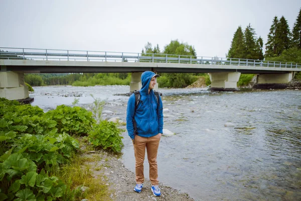 Erkek turist dağ nehrinin yanında duruyor.