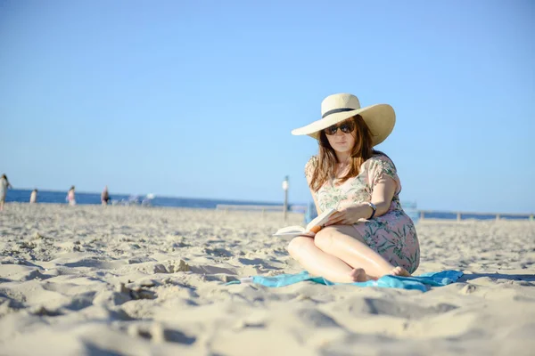 Retrato de una joven morena relajándose en la playa, leyendo un libro — Foto de Stock