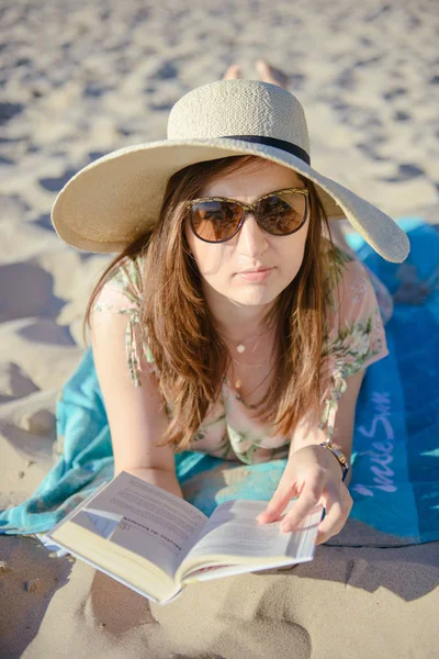 Retrato de uma jovem morena relaxando na praia, lendo um livro — Fotografia de Stock