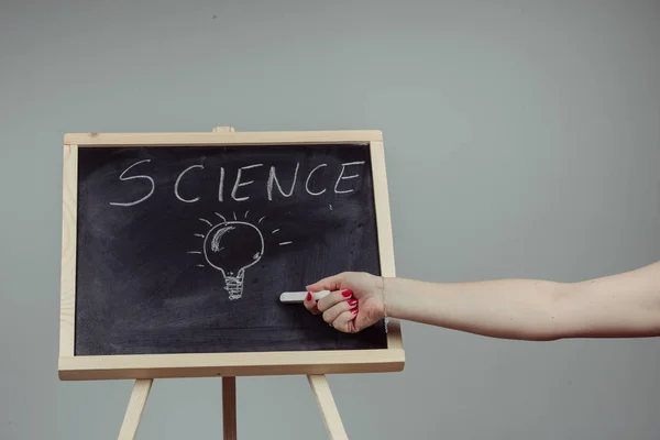 A teacher writing science, drawing chemistry elements on dark chalkboard by hand