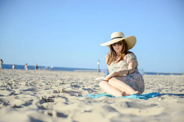 Retrato de una joven morena relajándose en la playa, leyendo un libro — Foto de Stock