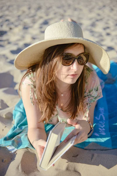 Retrato de uma jovem morena relaxando na praia, lendo um livro — Fotografia de Stock