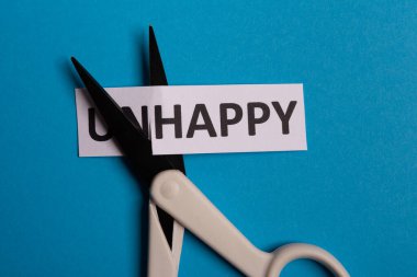 Mutsuz bir kart, 'un' ile kesilmiş kelime böylece 'mutlu' yazdı. Uzayı kopyala Mavi arka plan. Stüdyo çekimi