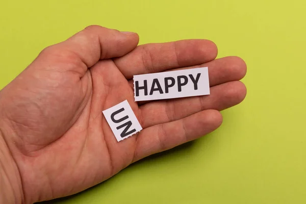 Рука людини тримає листівку з текстом нещасливим, вирізаючи слово "не", так що він написав "щасливий". Копіювати простір. Вапняний фон. Студійна стрілянина — стокове фото