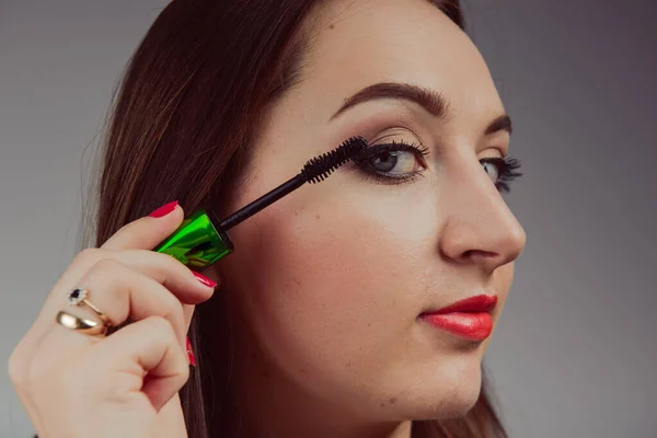 Skönhet modell tonårig flicka tittar i spegeln och tillämpa mascara gör. Vacker ung kvinna applicera makeup — Stockfoto