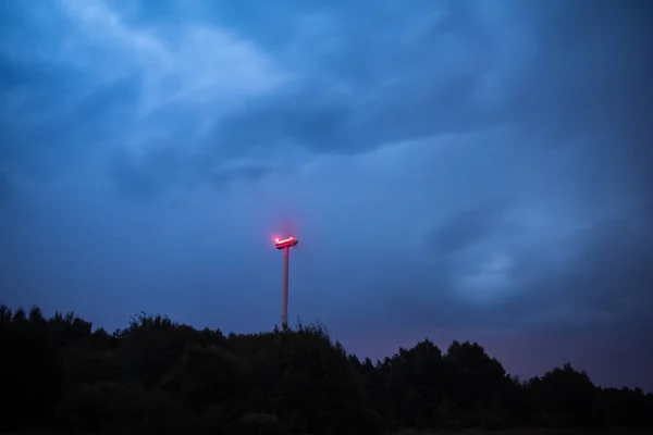 Turbinas de viento en unas dramáticas nubes azules oscuras en el cielo. Se acerca la tormenta. Luz de advertencia roja en el molino de viento . —  Fotos de Stock