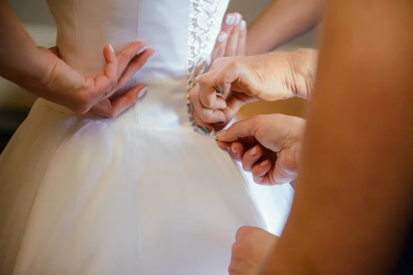 Bridesmaid helping slender bride lacing her wedding white dress, buttoning on delicate lace pattern with fluffy skirt on waist. Morning bridal preparation details newlyweds. Wedding day moments, wear. — Stock Photo, Image