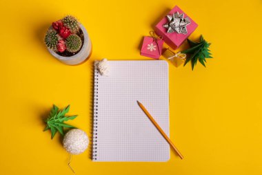 Hediye kutusu ve yeşil origami ağaçları sarı masa, masa üzerinde not defteri..