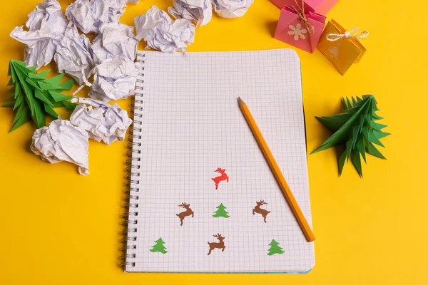 Caixa de presente e origami de papel verde árvores com bloco de notas na mesa amarela, mesa. Natal para fazer lista de texto — Fotografia de Stock