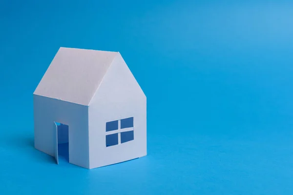 White family paper house over block of flats on blue background Stock Photo