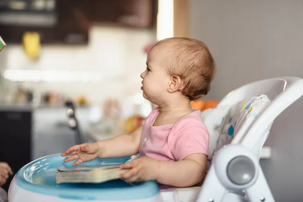 Niño rubio lindo se sienta en una silla de los niños en la cocina y comer un melocotón jugoso. Niña con una mirada penetrante —  Fotos de Stock