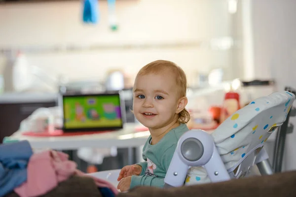 Niño rubio lindo se sienta en una silla de los niños en la cocina y comer un melocotón jugoso. Niña con una mirada penetrante —  Fotos de Stock