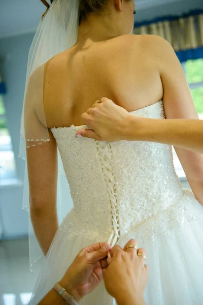 Damigella d'onore aiutare sposa snella allacciare il suo abito bianco di nozze, abbottonatura sul modello di pizzo delicato con gonna morbida in vita. Mattina sposa dettagli preparazione sposi. Momenti del giorno del matrimonio, indossare. — Foto Stock