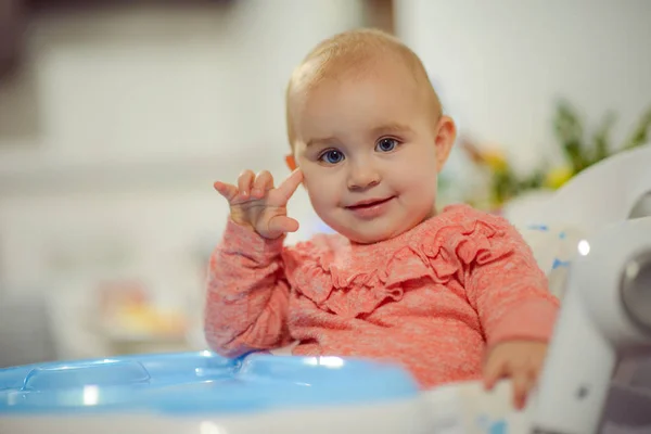 Niño rubio lindo se sienta en una silla de los niños en la cocina y comer un melocotón jugoso. Niña con una mirada penetrante —  Fotos de Stock