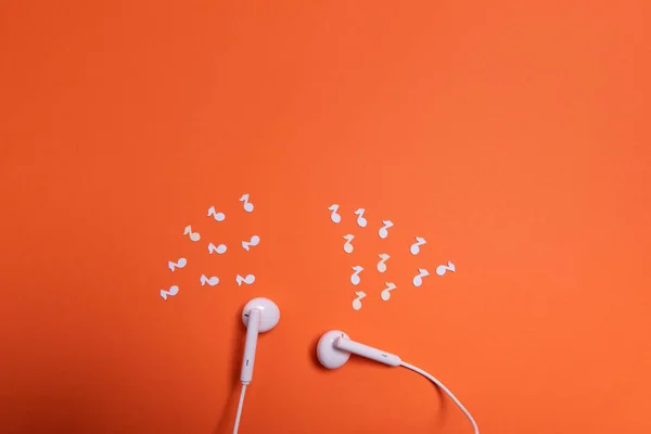 white earphones and white paper notes on orange background. view from above.