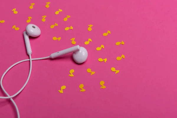 Fones de ouvido brancos e notas de papel amarelo no fundo rosa. vista de cima . — Fotografia de Stock