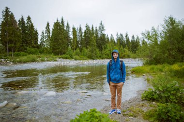 Erkek turist dağ nehrinin yanında duruyor.