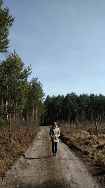 Egy fiatal nő sétál el egyedül egy erdei úton napszemüvegben. Március elején, tavasszal. — Stock Fotó
