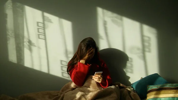 Sad woman making a phone call on the bed. Depressed, evastated woman sitting in bed and holding the phone. 로열티 프리 스톡 이미지