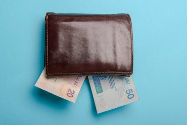 Kahverengi adam deri cüzdanı ve mavi arka planda para faturaları.