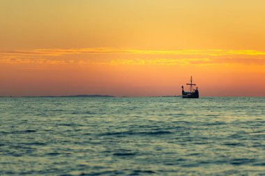 Çakıl taşlı sahilde eski bir balıkçı teknesinin üzerinde güzel bir gündoğumu, klasik efekt.
