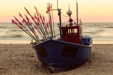 Çakıl taşlı sahilde eski bir balıkçı teknesinin üzerinde güzel bir gündoğumu, klasik efekt.