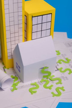 Kağıt gökdelenler, Amerikan dolarları, ev projeleri planı ve mavi arkaplan kağıdındaki planlar. Minimalist ve basit bir kavram, tarz. Yatay oryantasyon. Yukarıdan bak. Boşluğu kopyala.