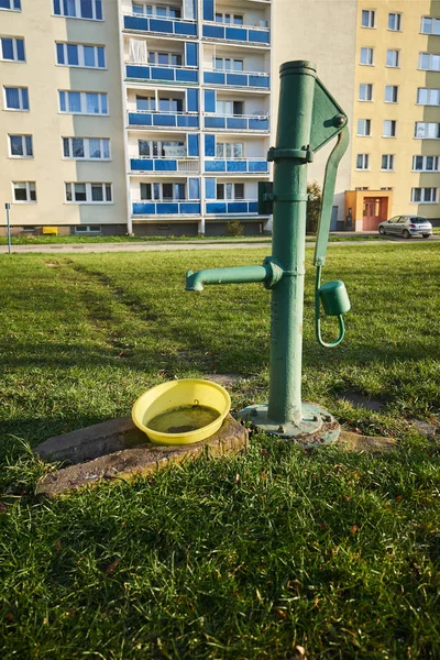 An old, cast-iron pump in front of a modern apartment block in Poznan
