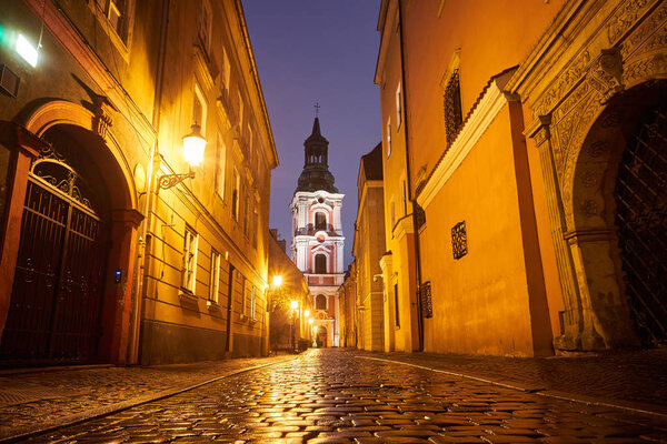 Cobbled street and belfry of the baroque historic church at night in Poznan