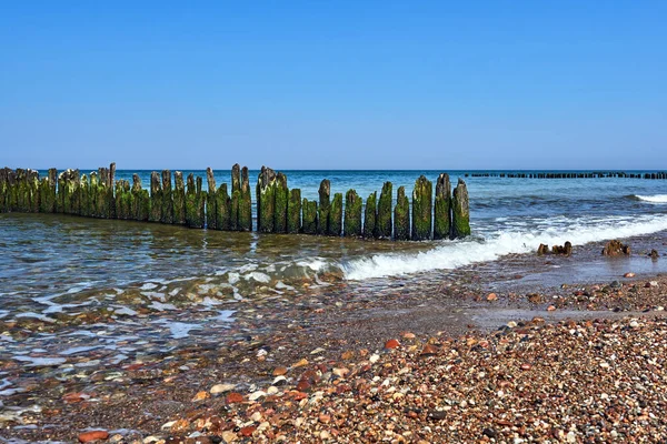 ポーランドのバルト海沿岸の石のビーチと木製の防波堤 — ストック写真